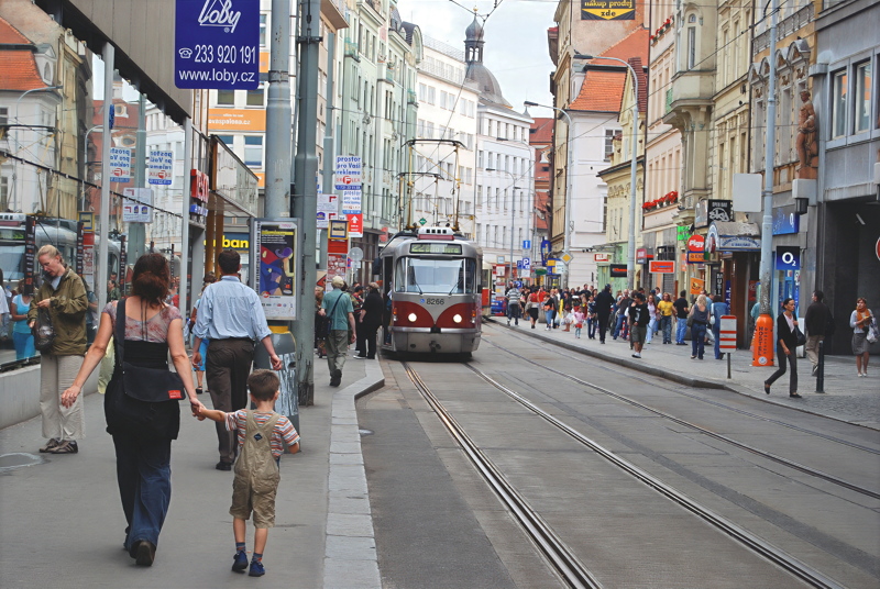 1 - A classic red-and-white Tatra T3 tram operating on line 22 along a historic, bustling street in Prague with pedestrians walking